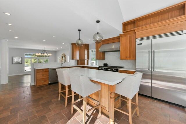 kitchen with kitchen peninsula, wall chimney exhaust hood, hanging light fixtures, and stainless steel appliances