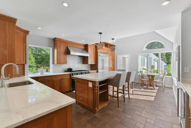 kitchen with pendant lighting, a kitchen island, wall chimney range hood, high end appliances, and sink