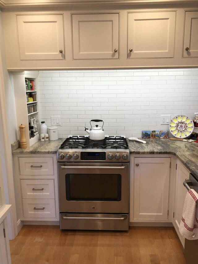 kitchen featuring light wood-type flooring, stainless steel appliances, stone counters, and decorative backsplash