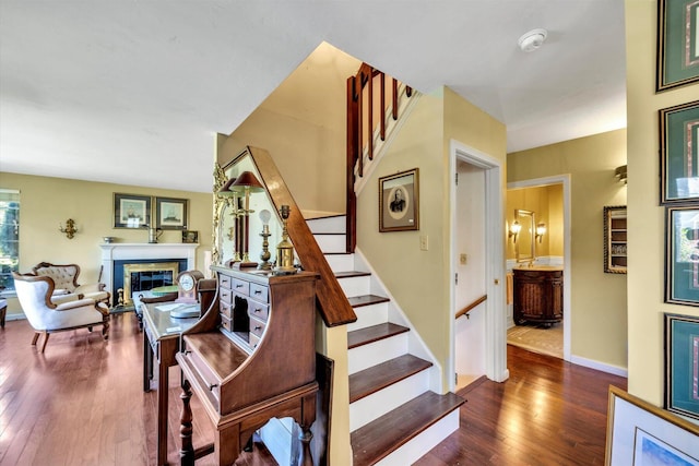 staircase featuring a glass covered fireplace, baseboards, and wood finished floors