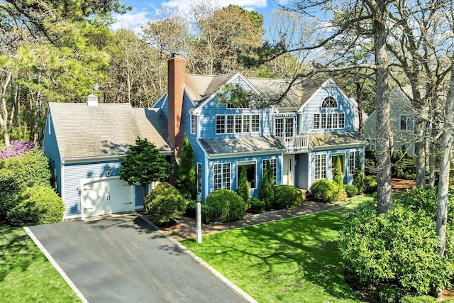 view of front of property with aphalt driveway, a chimney, a garage, a balcony, and a front lawn