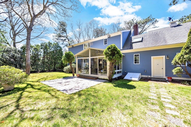 rear view of house featuring a sunroom, a patio area, a lawn, and a chimney