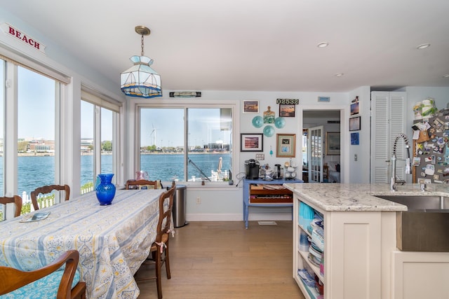 dining room featuring light wood-type flooring, a water view, healthy amount of natural light, baseboards, and recessed lighting