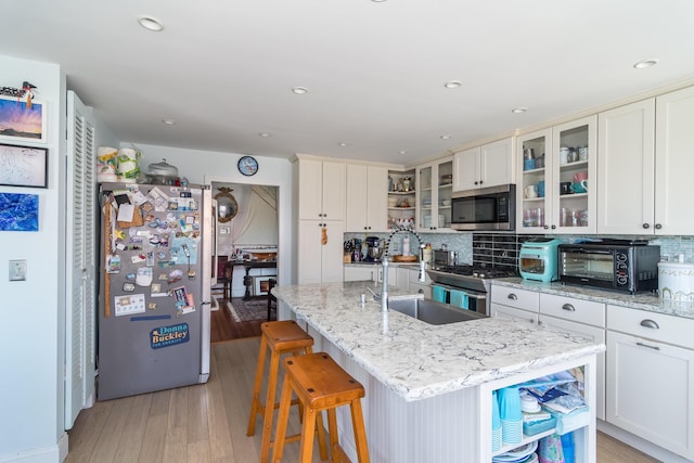 kitchen featuring appliances with stainless steel finishes, a sink, tasteful backsplash, light wood finished floors, and recessed lighting