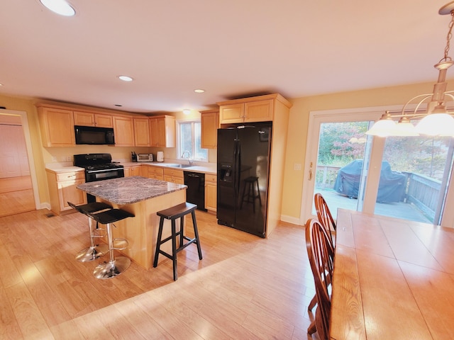 kitchen with a kitchen breakfast bar, light hardwood / wood-style flooring, black appliances, and a center island