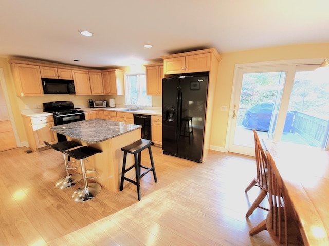 kitchen with light wood-type flooring, a center island, a breakfast bar, and black appliances