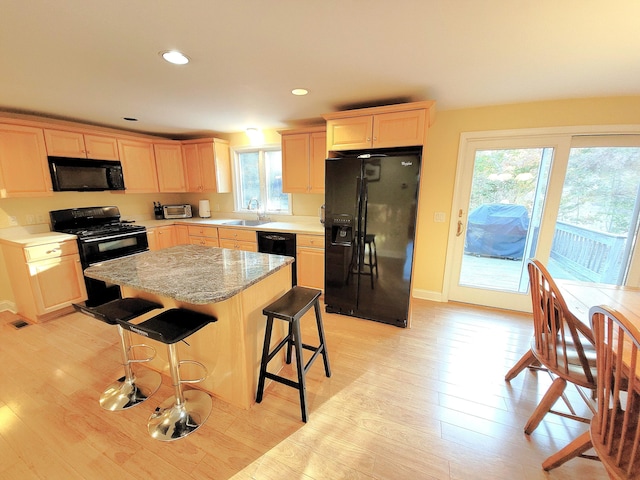 kitchen featuring a kitchen island, sink, a kitchen bar, light hardwood / wood-style floors, and black appliances