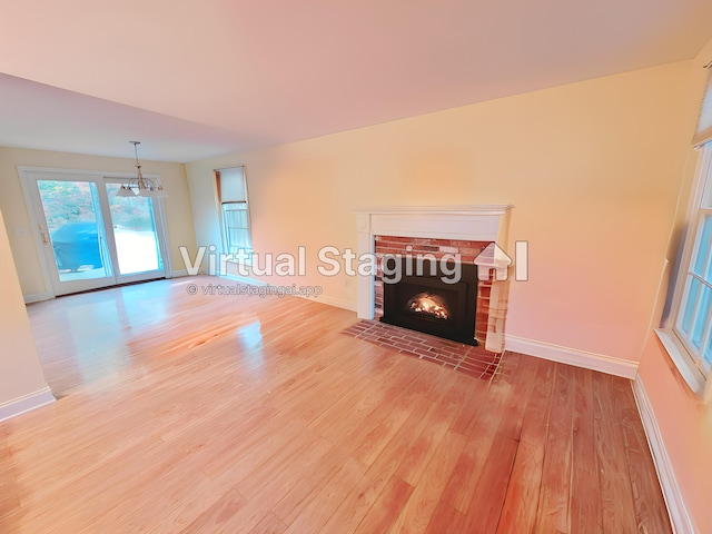 unfurnished living room with a brick fireplace, a notable chandelier, and light hardwood / wood-style flooring