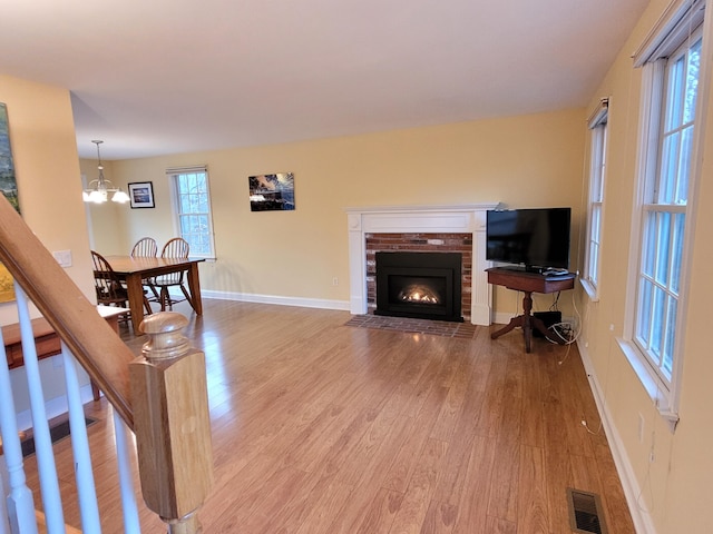 living room featuring a brick fireplace, an inviting chandelier, and light hardwood / wood-style floors