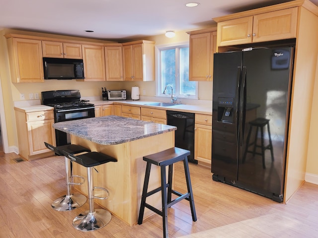 kitchen with a breakfast bar, sink, light hardwood / wood-style flooring, and black appliances