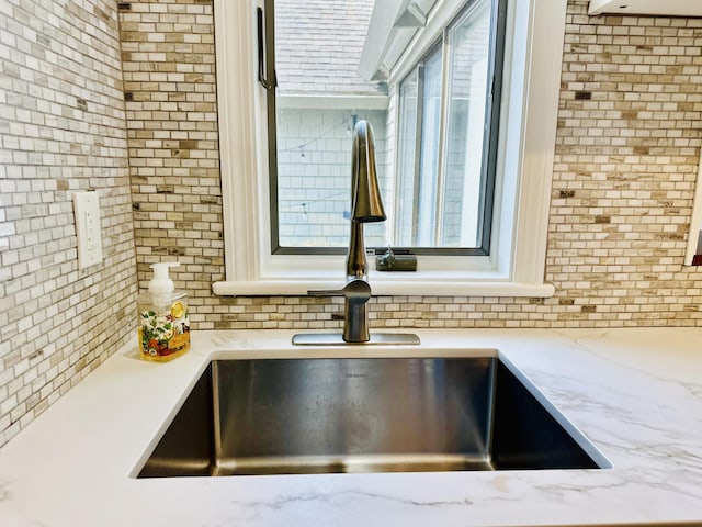 interior details with light stone counters, backsplash, and a sink