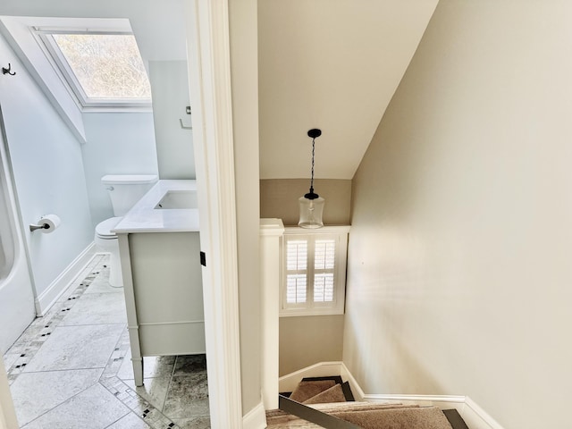 bathroom with a skylight, toilet, vanity, and baseboards