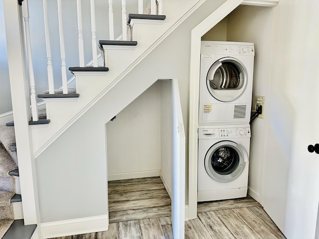 laundry room with stacked washer / dryer, laundry area, baseboards, and wood finished floors