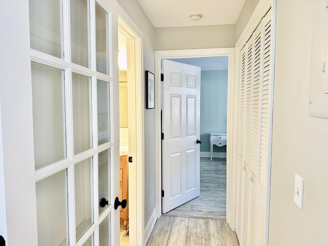 corridor featuring french doors, baseboards, and light wood-style floors