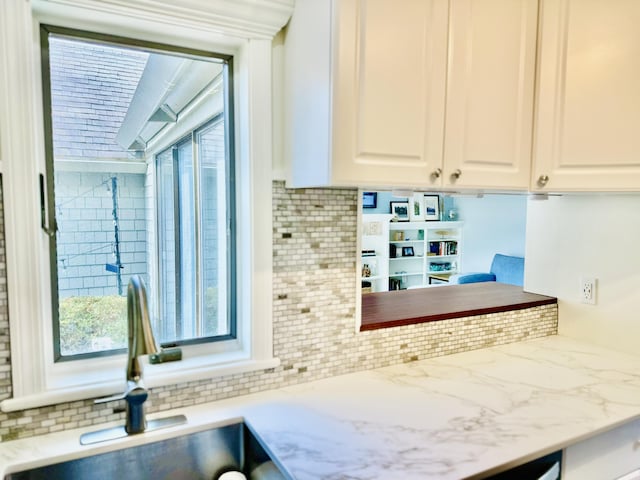 kitchen with decorative backsplash, white cabinets, light stone countertops, and a sink