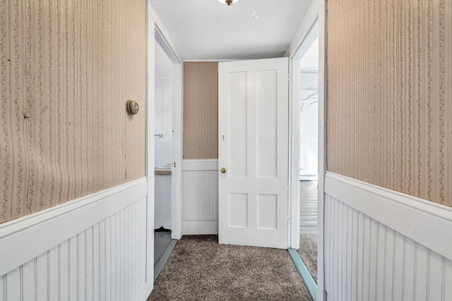 hall with dark colored carpet, wainscoting, and wallpapered walls