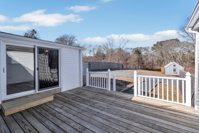 wooden terrace with a storage unit, fence, and an outbuilding