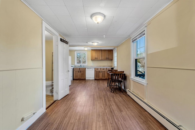 kitchen with brown cabinets, light countertops, baseboard heating, wood finished floors, and dishwasher