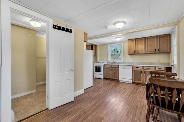 kitchen featuring white appliances, wood finished floors, a sink, light countertops, and brown cabinets