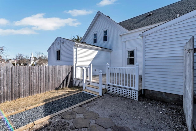 rear view of property featuring a deck, a shingled roof, and fence