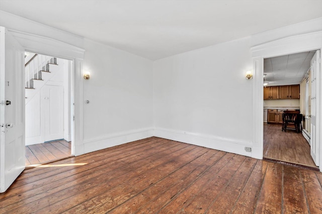 unfurnished room with dark wood-type flooring, a baseboard heating unit, baseboards, and stairs