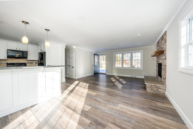 kitchen with white cabinets, black appliances, a fireplace, a breakfast bar, and crown molding