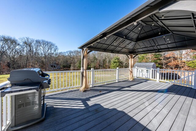 wooden terrace with a gazebo, a shed, and area for grilling