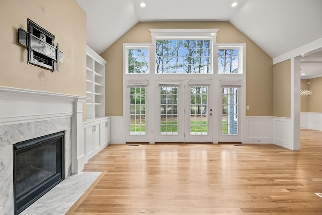 7 Nicklaus Way, Mashpee, MA 02649 - unfurnished living room featuring a high end fireplace, high vaulted ceiling, a wainscoted wall, light wood finished floors, and a decorative wall