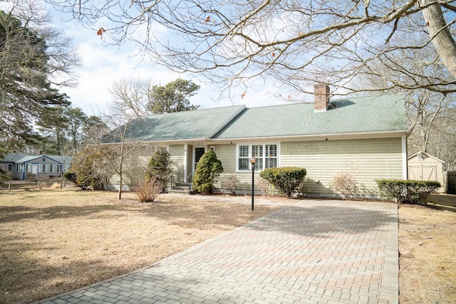 view of front of house with a shingled roof, a chimney, an outdoor structure, a front lawn, and a storage shed