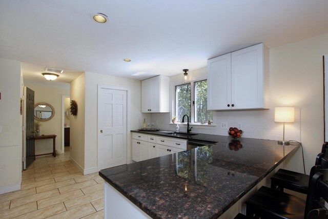 473 Thousand Oaks Dr, Brewster, MA 02631 - kitchen featuring a sink, dark stone counters, white cabinets, a peninsula, and a kitchen breakfast bar