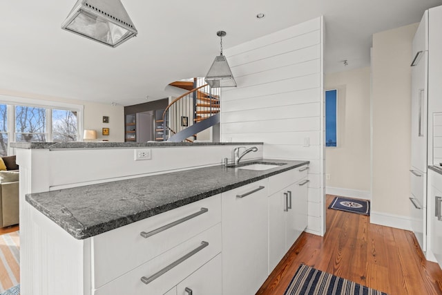 kitchen with white cabinetry, hanging light fixtures, sink, dark hardwood / wood-style flooring, and dark stone counters