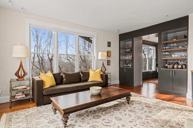 living room with built in shelves, a healthy amount of sunlight, bar area, and dark hardwood / wood-style flooring