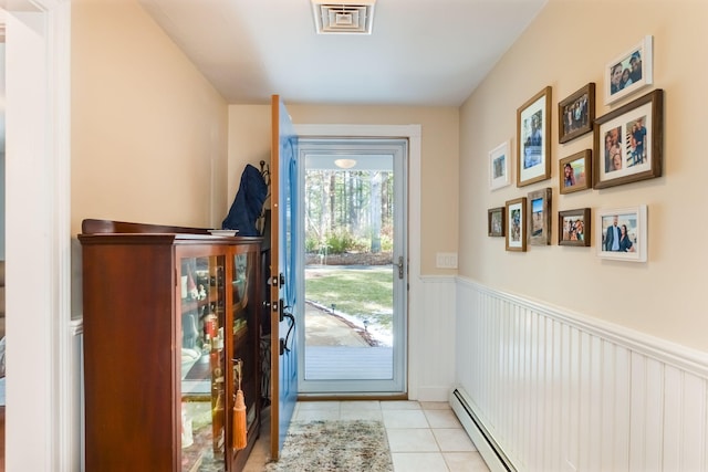 doorway with tile patterned flooring, visible vents, baseboard heating, and wainscoting