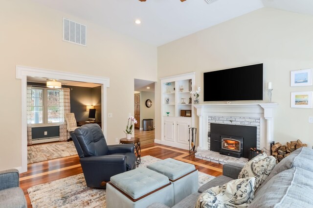 living room with visible vents, a ceiling fan, a baseboard heating unit, wood finished floors, and lofted ceiling