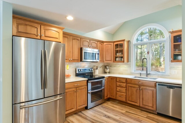 kitchen with a sink, stainless steel appliances, light countertops, glass insert cabinets, and lofted ceiling