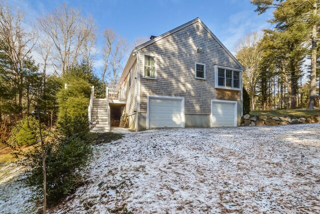 snow covered property featuring a garage, gravel driveway, and stairs