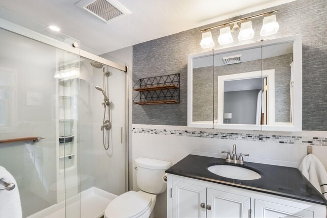 bathroom featuring visible vents, toilet, a stall shower, tile walls, and vanity