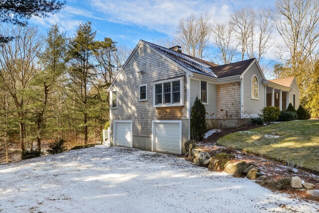 view of side of home featuring an attached garage, a chimney, driveway, and a yard