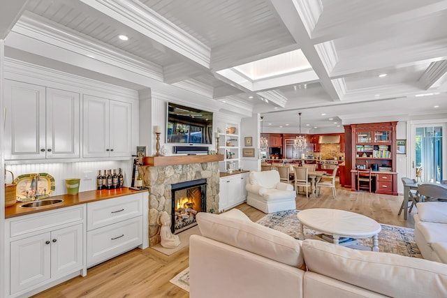 living room with beamed ceiling, crown molding, a stone fireplace, and sink