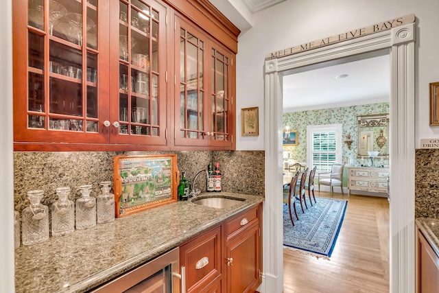 kitchen with sink, backsplash, light stone counters, crown molding, and light hardwood / wood-style flooring