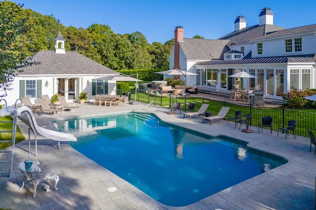 view of swimming pool featuring grilling area, a water slide, an outdoor structure, and a patio area