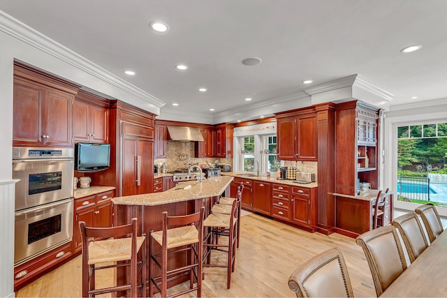 kitchen featuring an island with sink, sink, wall chimney range hood, and a kitchen bar