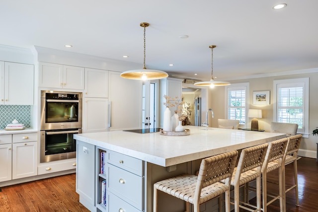 kitchen featuring light stone countertops, white cabinets, pendant lighting, an island with sink, and double oven