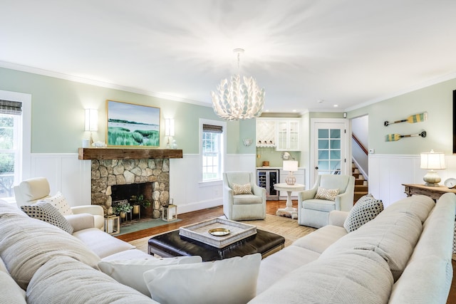 living room with beverage cooler, a stone fireplace, ornamental molding, a chandelier, and light hardwood / wood-style flooring