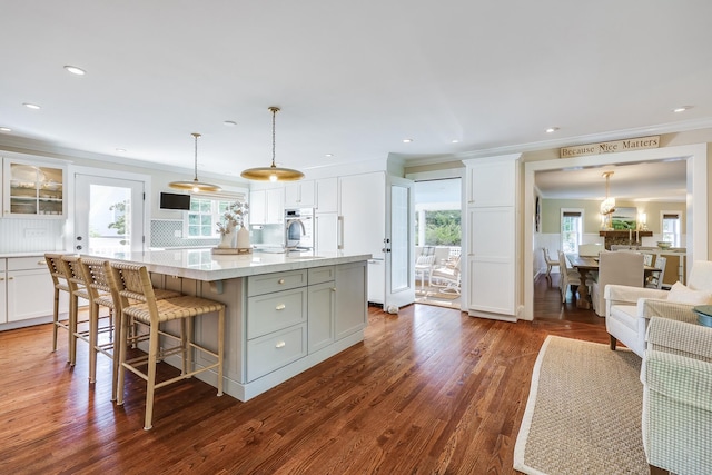 kitchen featuring pendant lighting, white cabinets, backsplash, dark hardwood / wood-style floors, and a kitchen island with sink