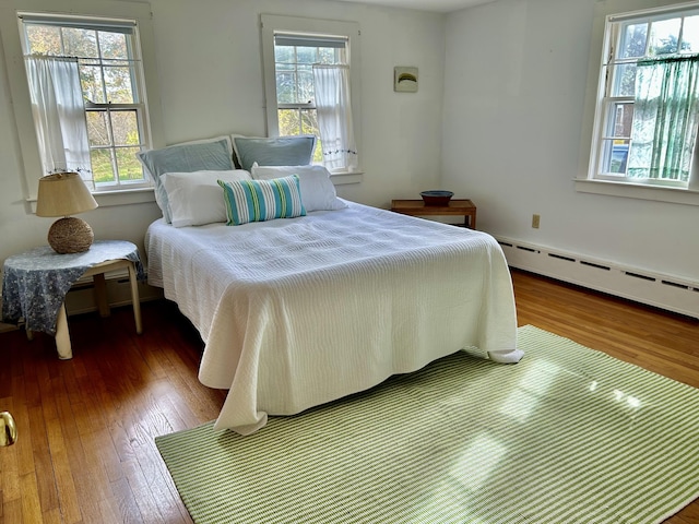 bedroom featuring a baseboard radiator, dark hardwood / wood-style floors, and multiple windows