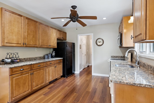 kitchen featuring wood finished floors, baseboards, freestanding refrigerator, light stone countertops, and stainless steel microwave