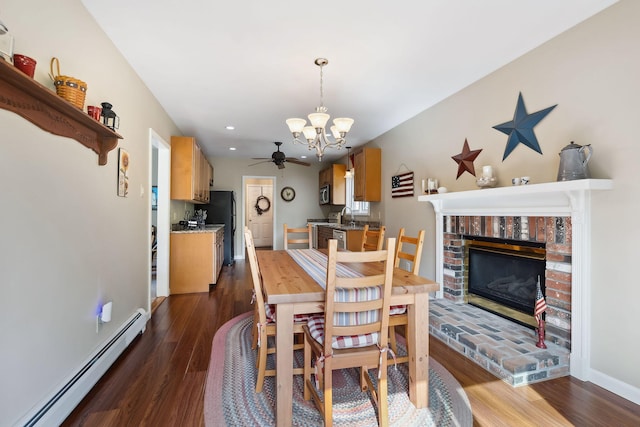 dining area featuring a brick fireplace, a baseboard heating unit, dark wood-type flooring, and ceiling fan with notable chandelier