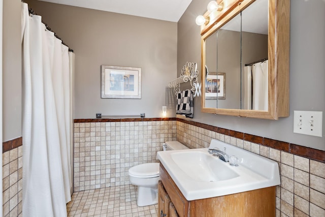 bathroom with toilet, a wainscoted wall, tile patterned flooring, vanity, and tile walls