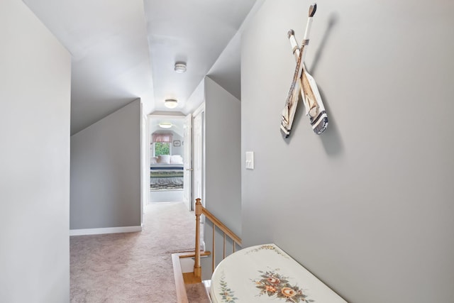 hall with carpet, baseboards, vaulted ceiling, and an upstairs landing